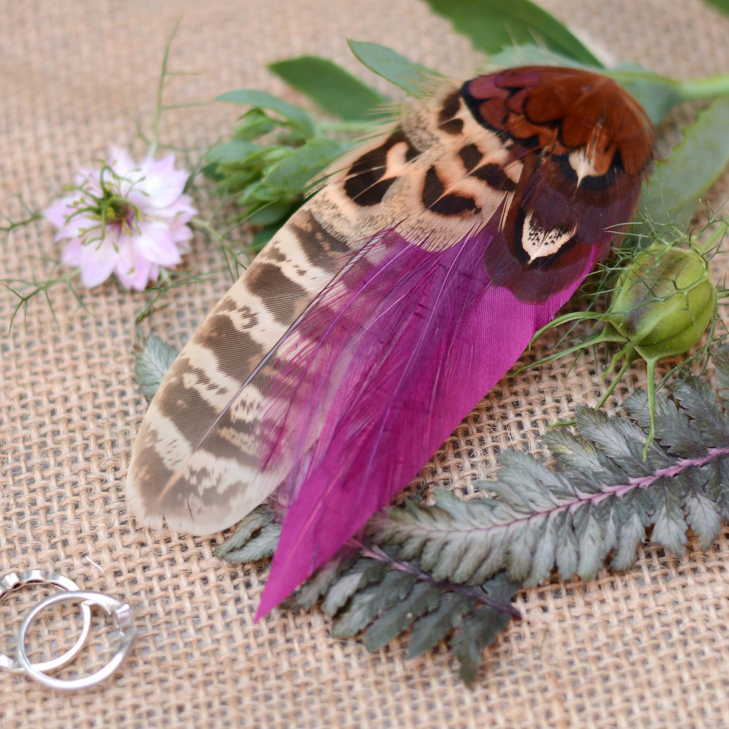 Two pheasant feather hair clip fascinators with vibrant purple and brown patterns on laying across greenery