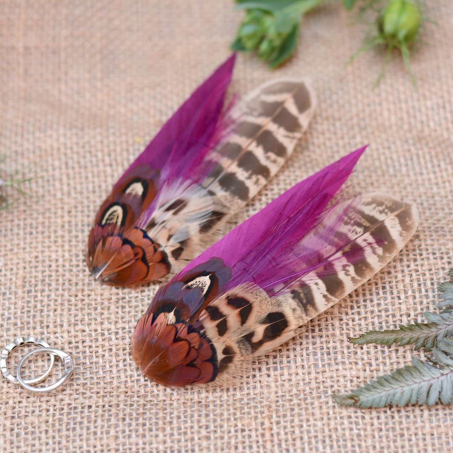 Two pheasant feather hair clip fascinators with vibrant purple and brown patterns on a textured fabric background.
