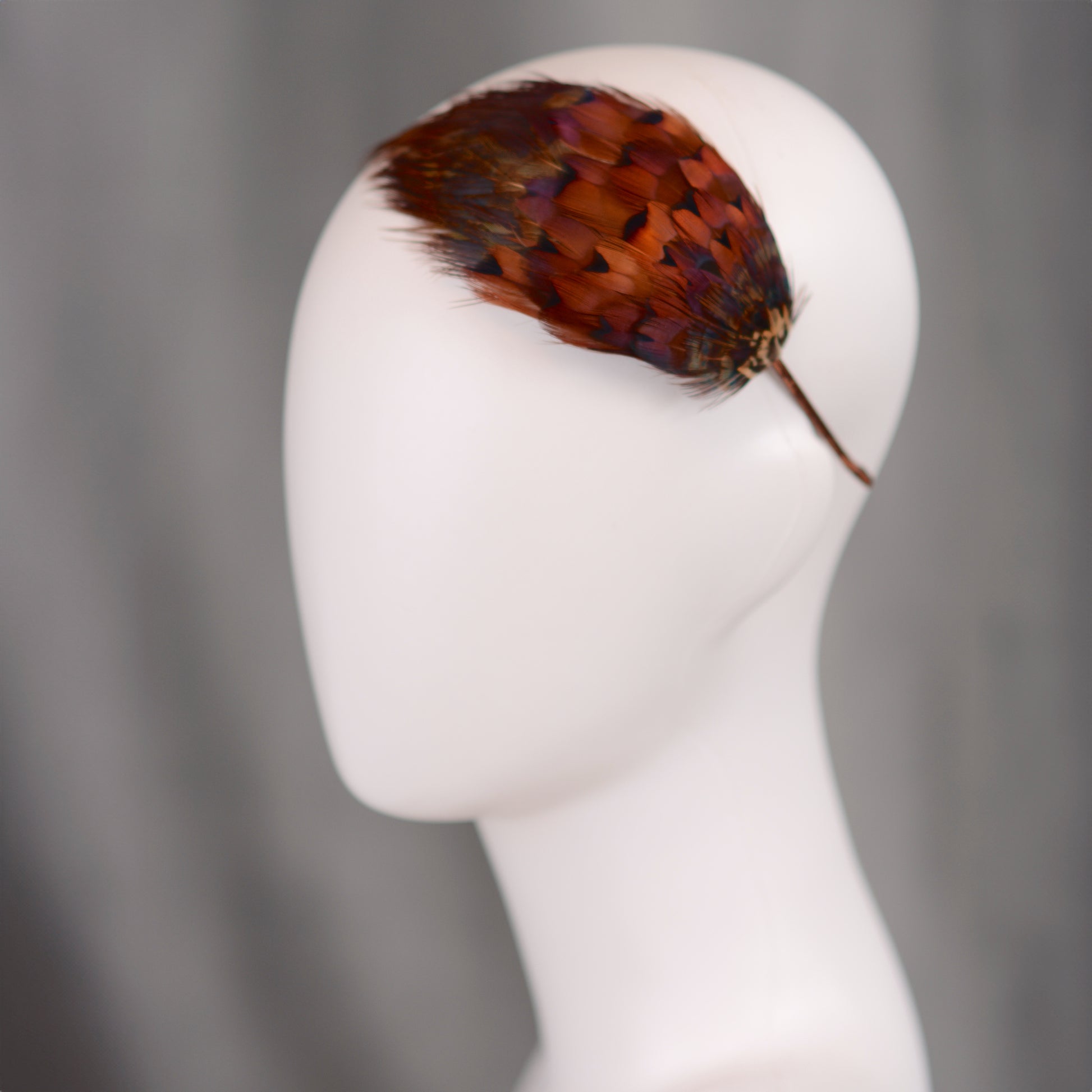 A feather hair accessory featuring real natural pheasant feathers in glowing amber and copper. Mounted on a headband covered in brown ribbon. ideal accessory for autumn / fall weddings and countryside events