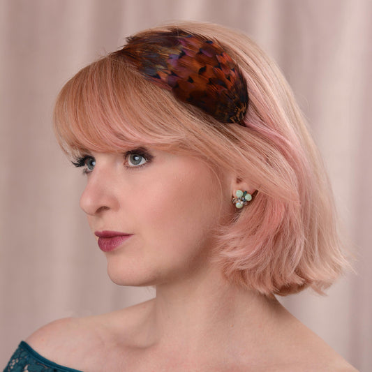 A woman with a pink bob wears a pheasant feather headband hair accessory with glowing amber pheasant feathers