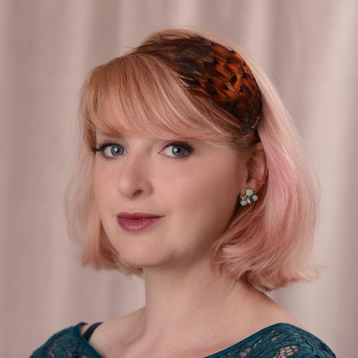 A woman with a pink bob wears a pheasant feather headband hair accessory with glowing amber pheasant feathers