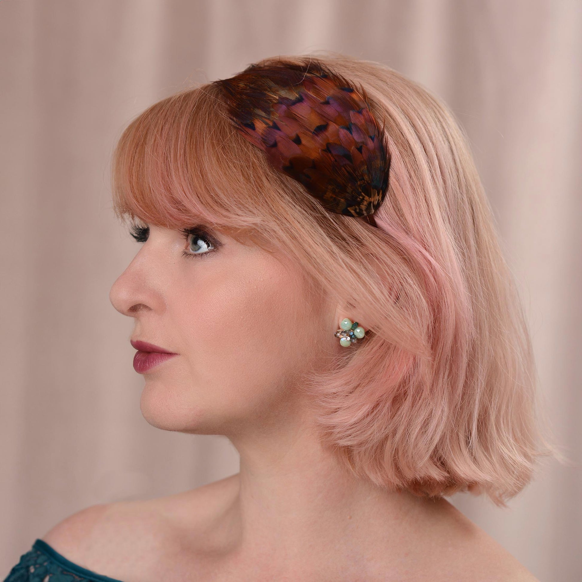 A woman with a pink bob wears a pheasant feather headband hair accessory with glowing amber pheasant feathers