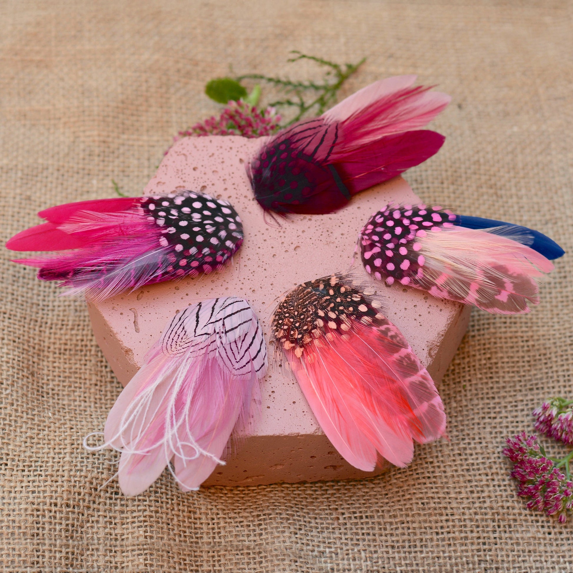 Decorative feather hair clips on a pink block with a burlap background
