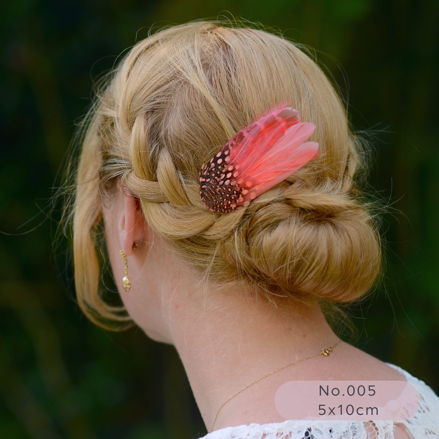 Woman with braided hair and a coral  pink feather hair accessory against a blurred green background