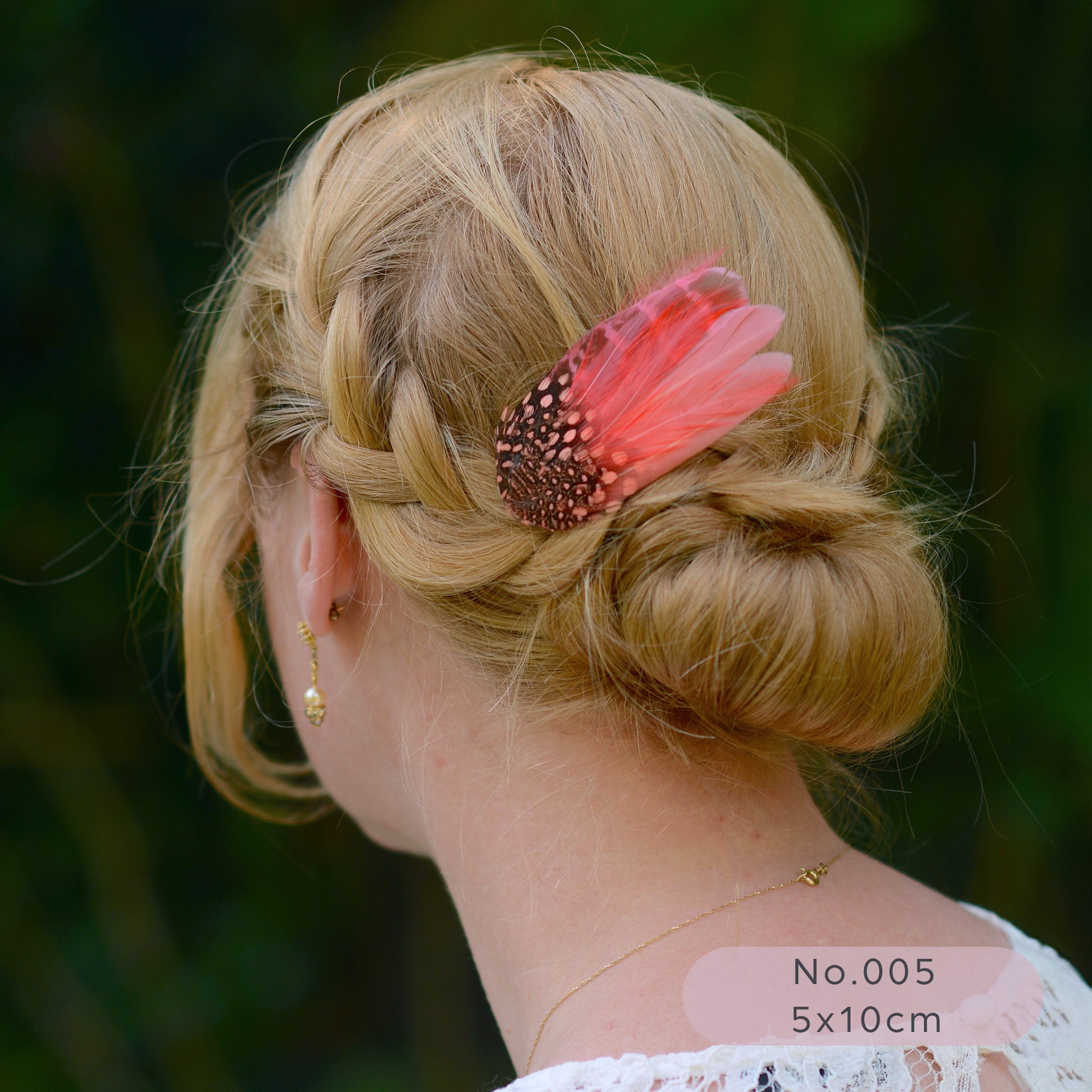 Woman with braided hair and a coral  pink feather hair accessory against a blurred green background