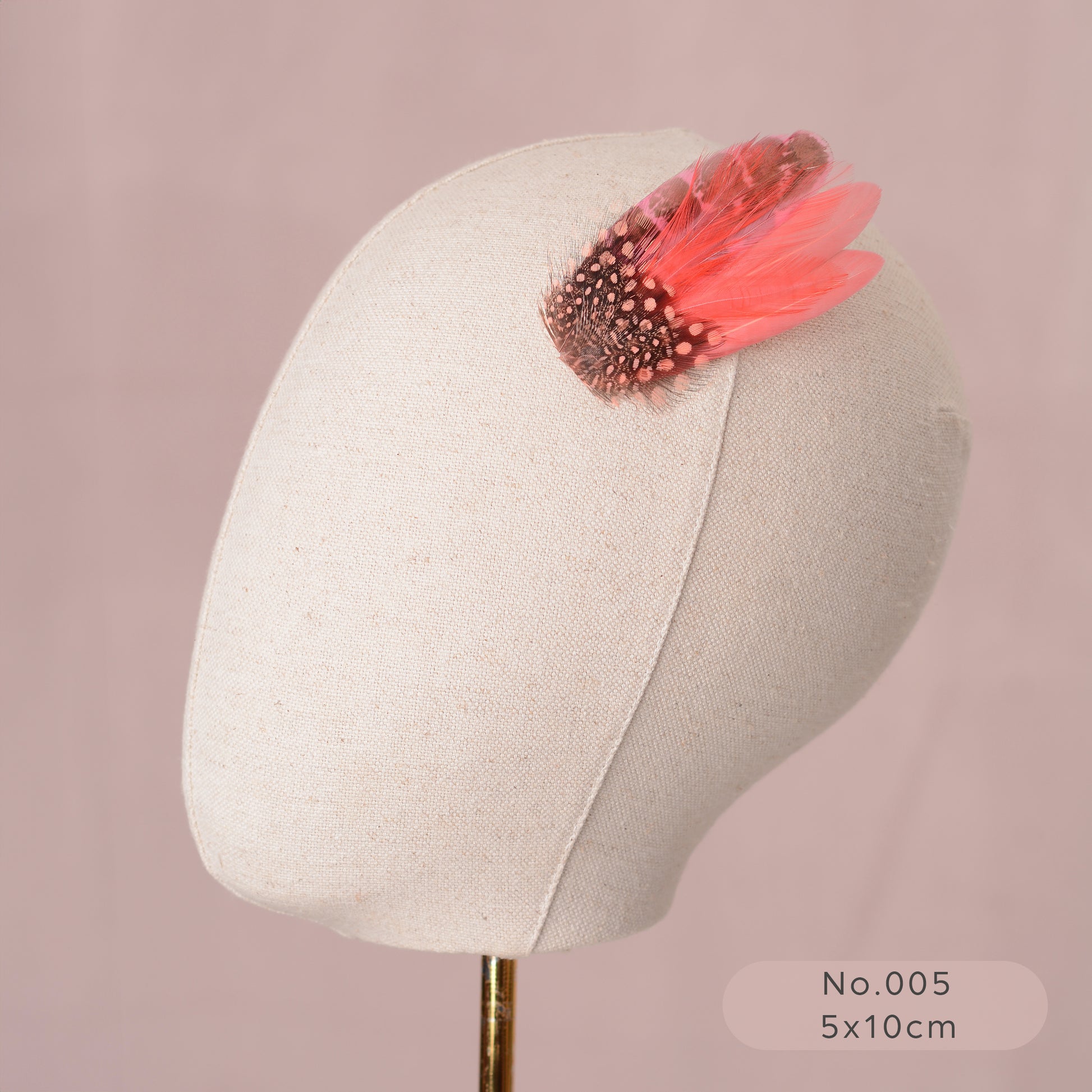 Mannequin head with a decorative coral pink feather hair clip on a pink background