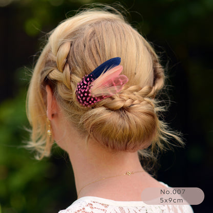 Person with braided hair and decorative pink and navy blue feather hair clip against a blurred green background