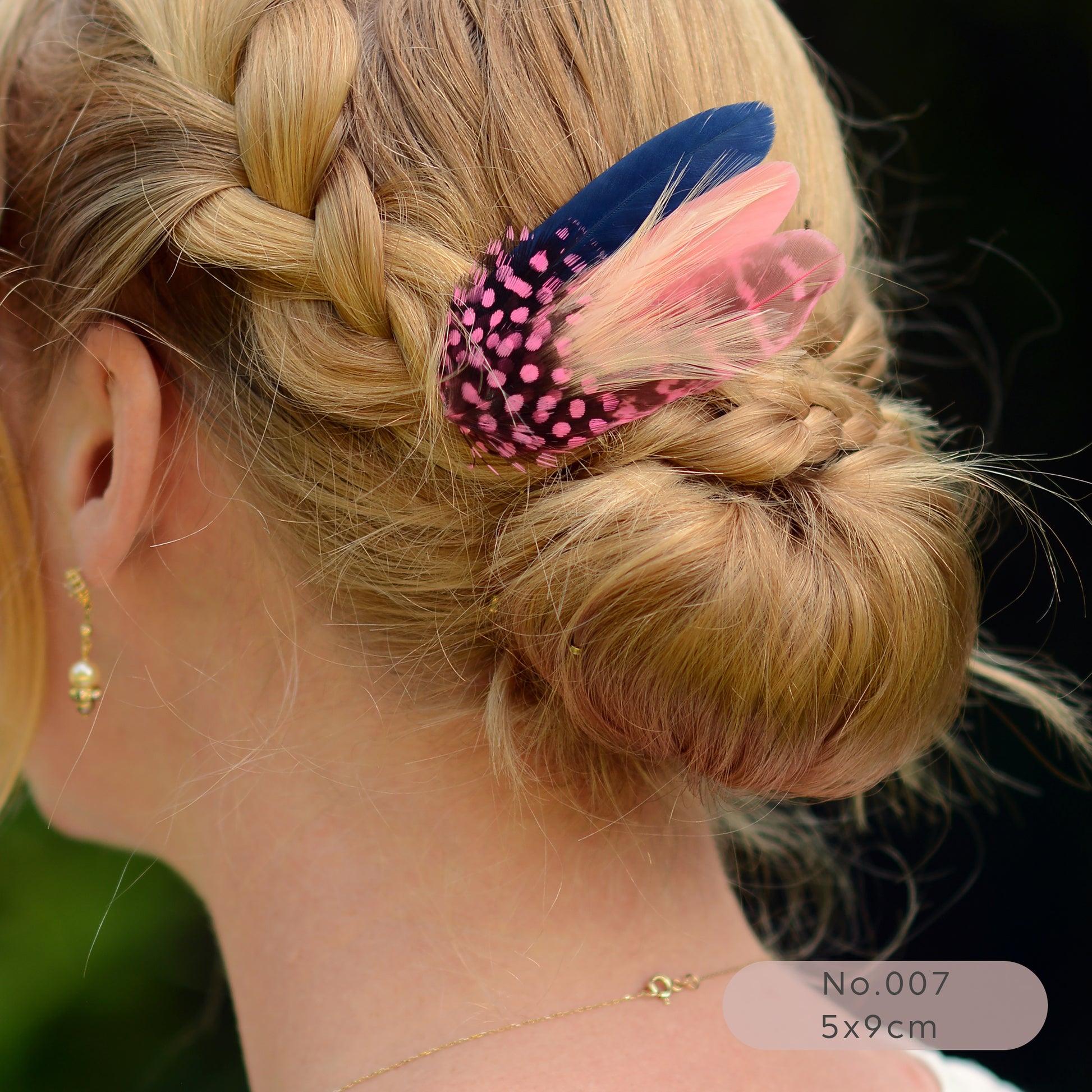 Close-up of a braided hairstyle with a decorative pink and navy blue feather hair clip on a dark background