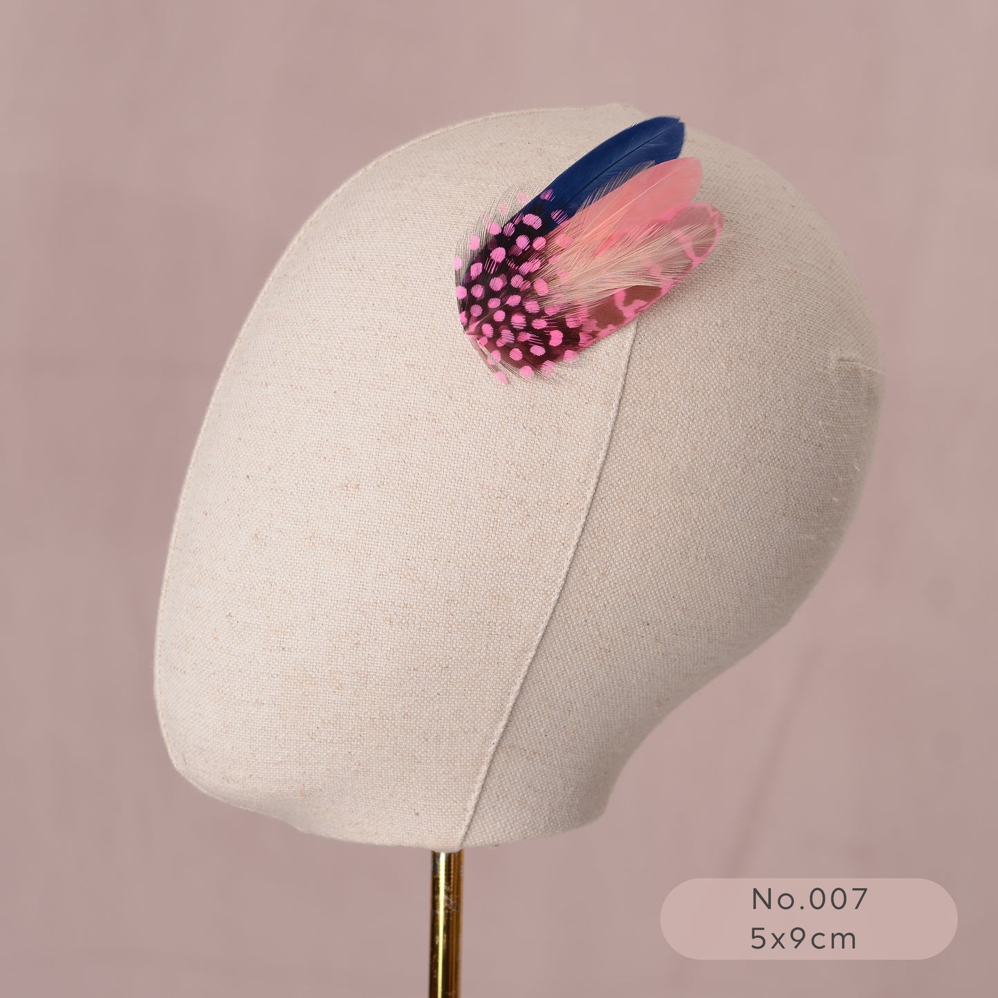 Mannequin head with a decorative pastel pink and navy blue feather hair clip on a pink background