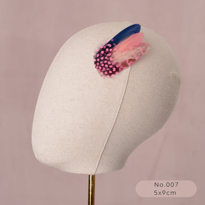 Mannequin head with a decorative pastel pink and navy blue feather hair clip on a pink background