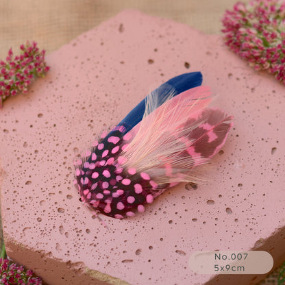 Decorative feather hair clip in pin and navy blue  on a pink textured background