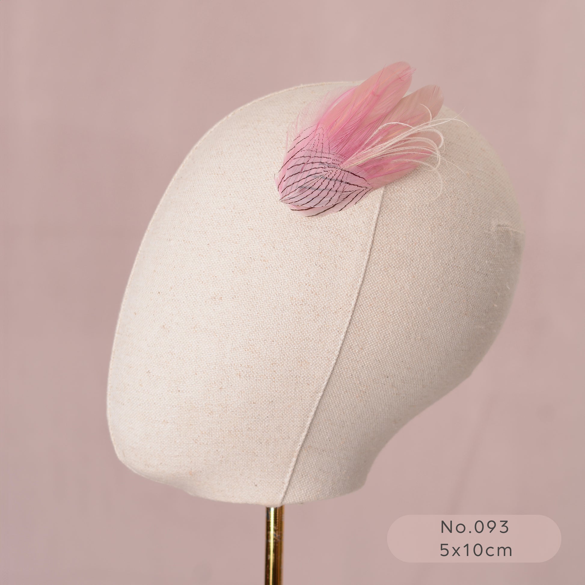 Mannequin head with a decorative pastel pink feather hair clip on a pink background