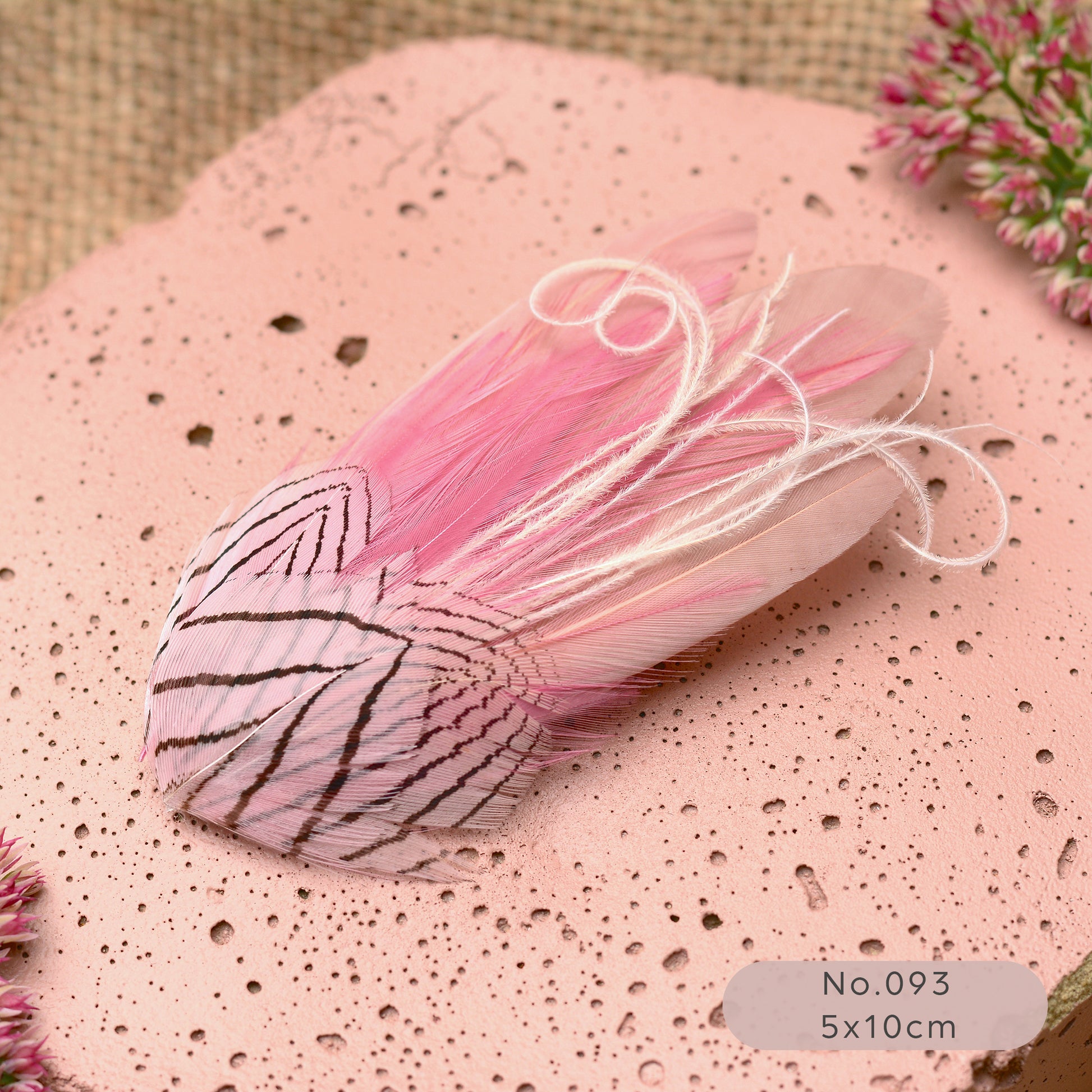 Decorative pastel pink feather hair clip on a textured pink surface with flowers in the background