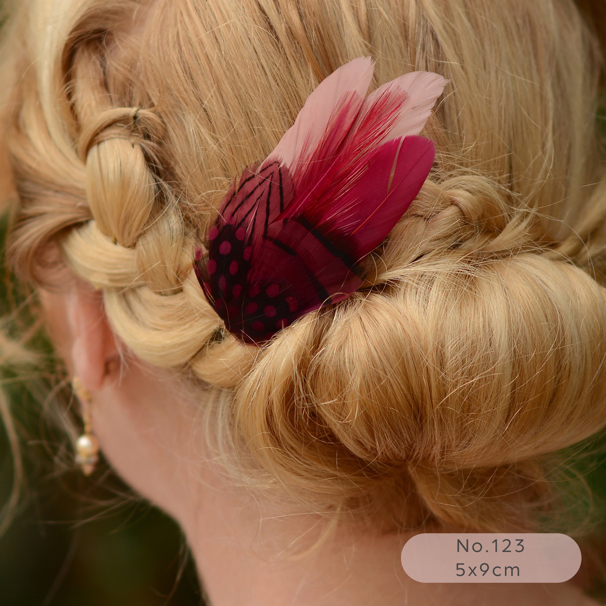 Close-up of a braided hairstyle with a pink and burgundy feather hair accessory.