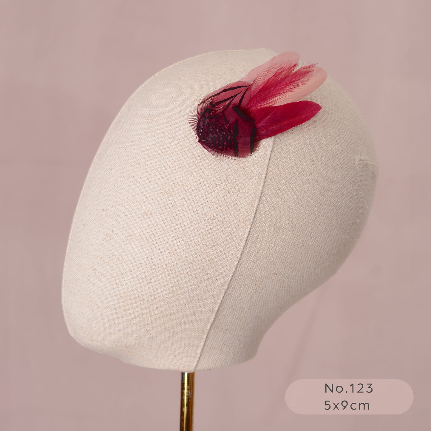 Mannequin head with a decorative pink and burgundy feather hair clip on a pink background