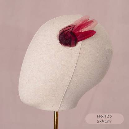 Mannequin head with a decorative pink and burgundy feather hair clip on a pink background