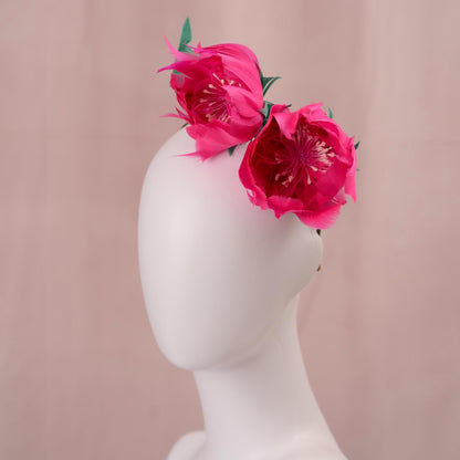 A wedding headpiece with vibrant pink goose feather peony flowers with green leaves styled on the side of a white mannequin head, set against a soft pink background.
