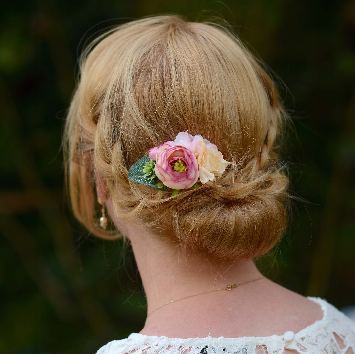 Woman with a styled hair bun adorned with pink flower hair accessory against a blurred natural background