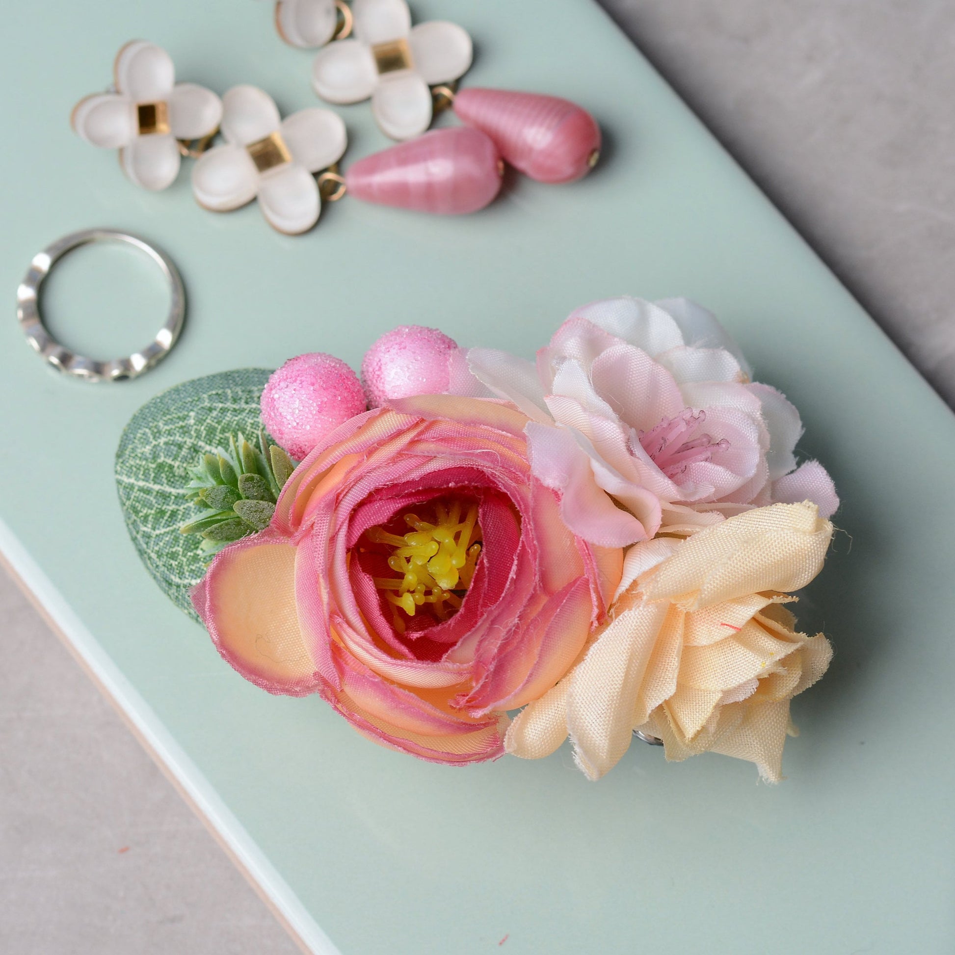 pink flower hair clip accessory on a mint green background with earrings and ring