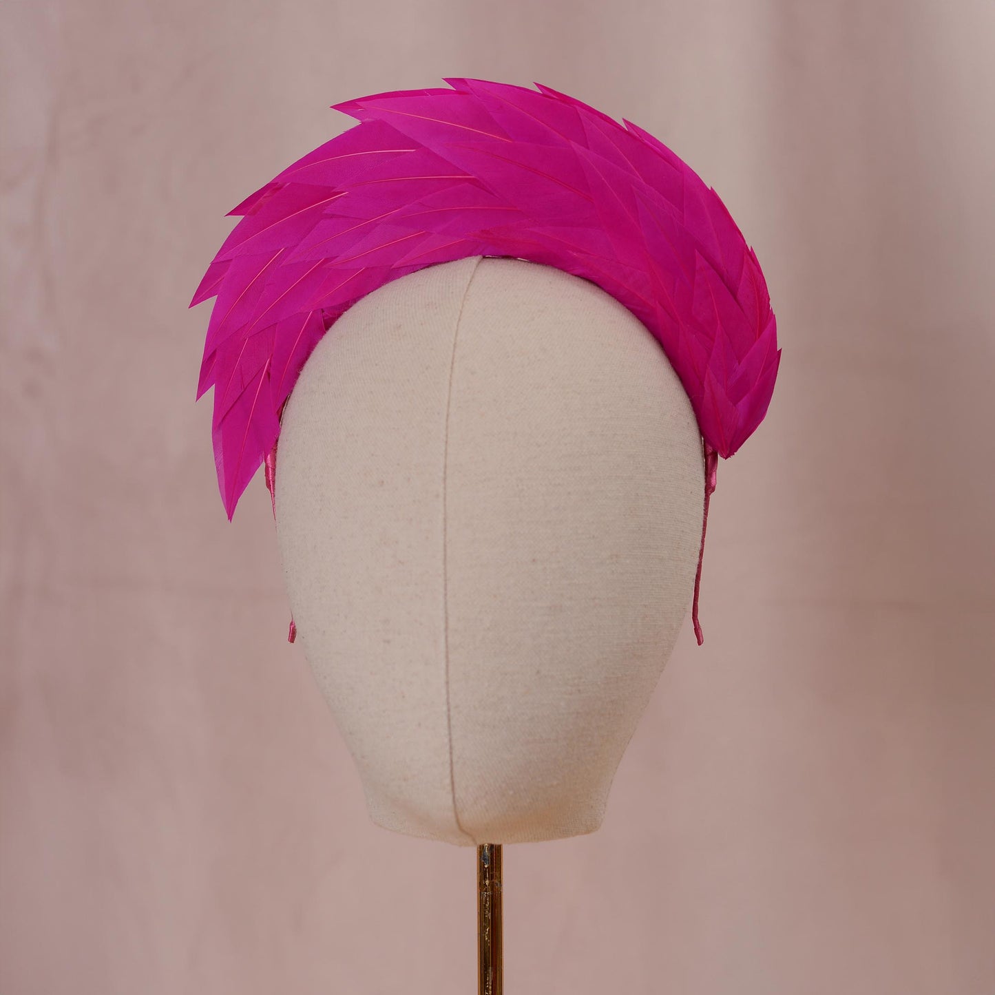 A bright fuchsia headband featuring a layered, fan-like arrangement of sharp pointed feathers that create a structured, semi-circular silhouette. The vibrant pink plumage is densely packed, extending upwards and outwards from the band.