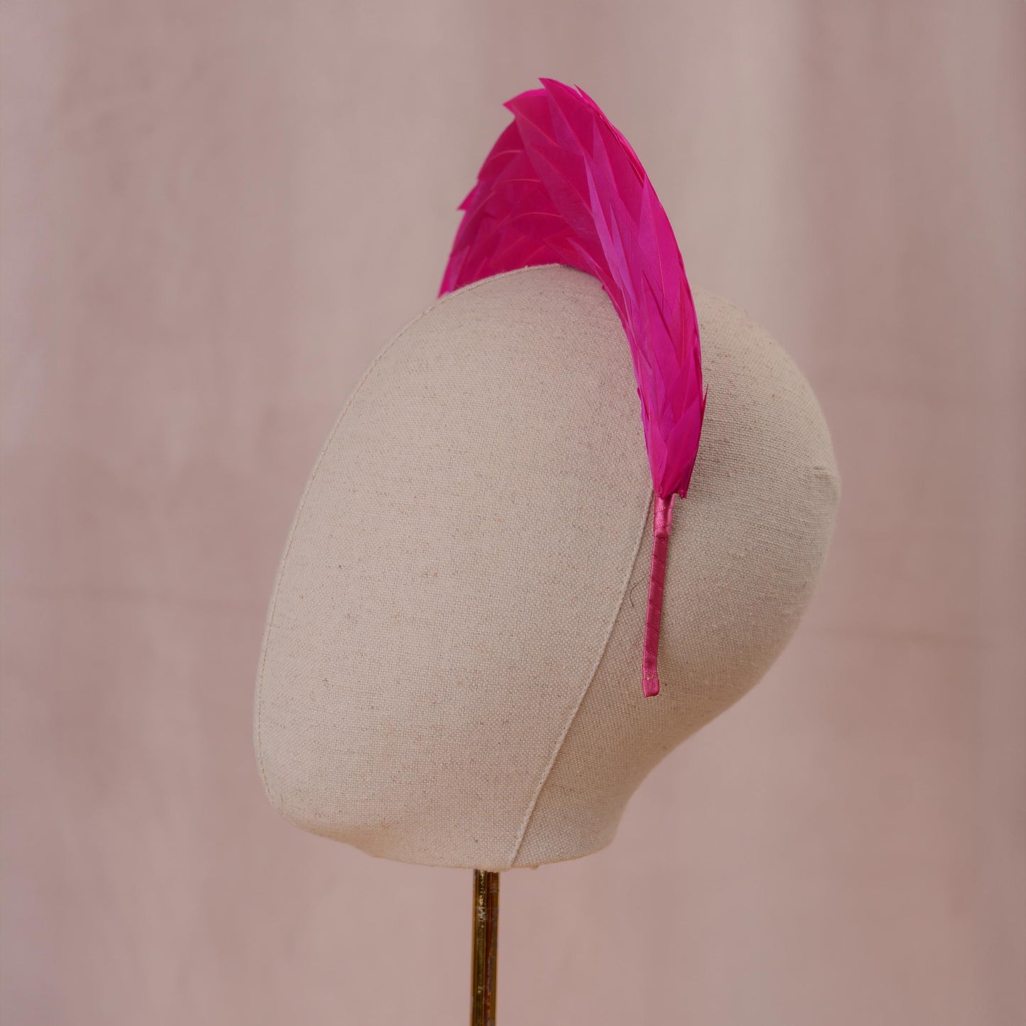  A bright hot pink headband featuring a tall, vertical arrangement of layered feathers that create a fan-like crest. The band itself is thin and wrapped in matching pink fabric, providing a secure base for the headpiece. Side view