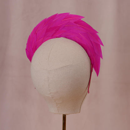 A bright pink feather headband or hair accessory displayed on a cream fabric mannequin head against a soft pink backdrop.