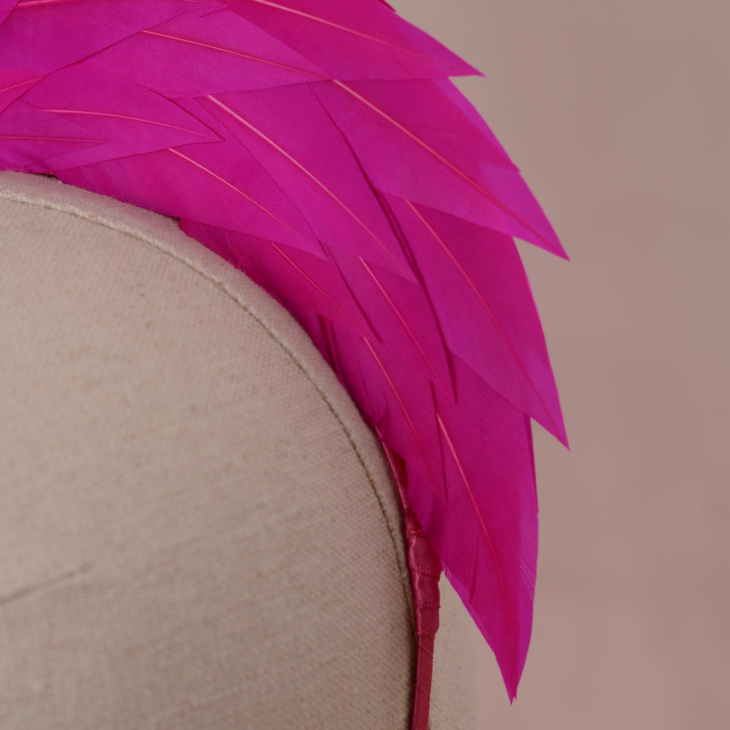 A close-up of a bright magenta feather accessory attached to a beige fabric-covered display form against a soft beige background.