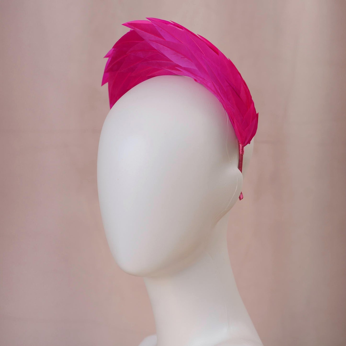 A bright hot pink feather headband displayed on a white mannequin head against a soft beige background.