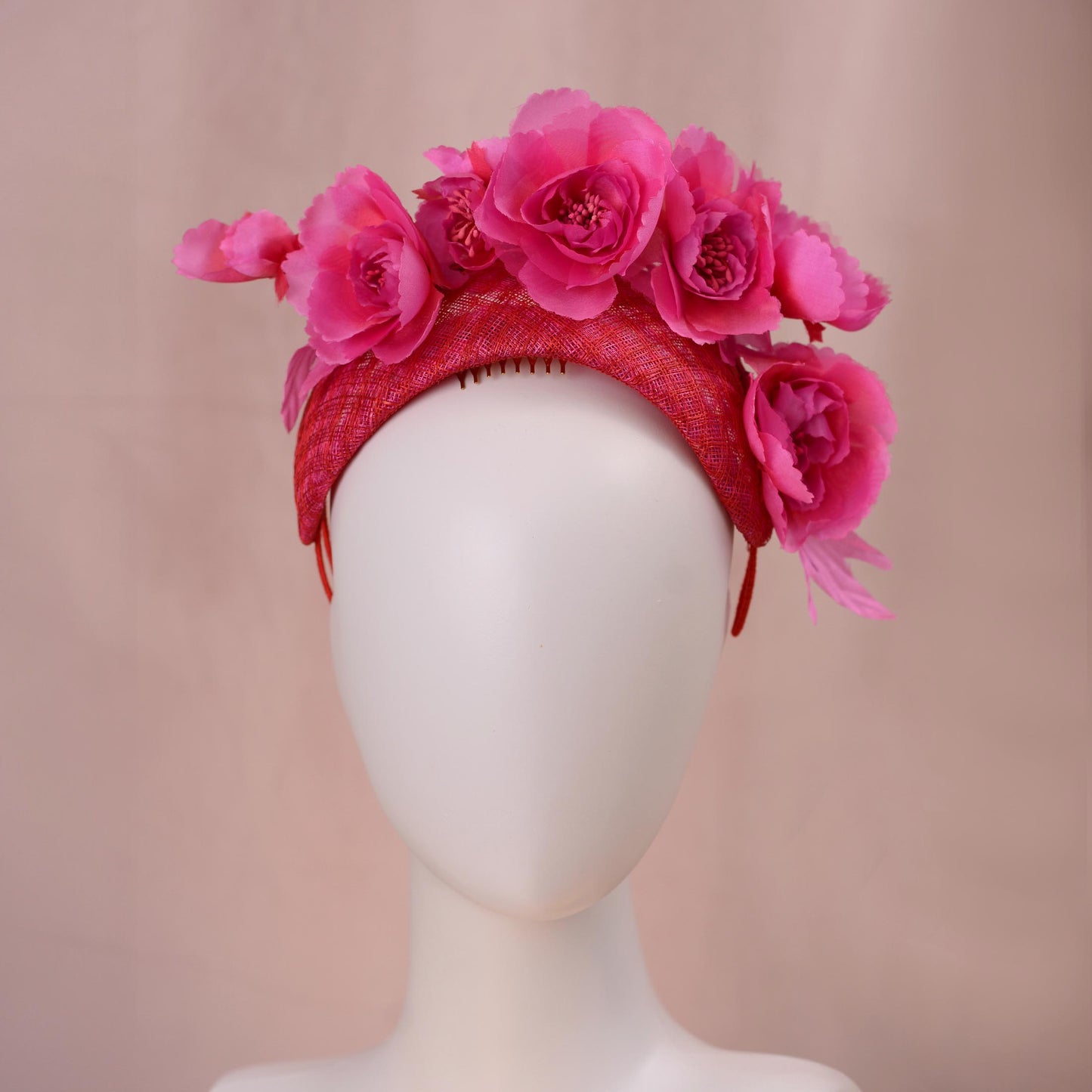 A bright pink and red silk floral fascinator headband displayed on a white mannequin head against a soft beige background.