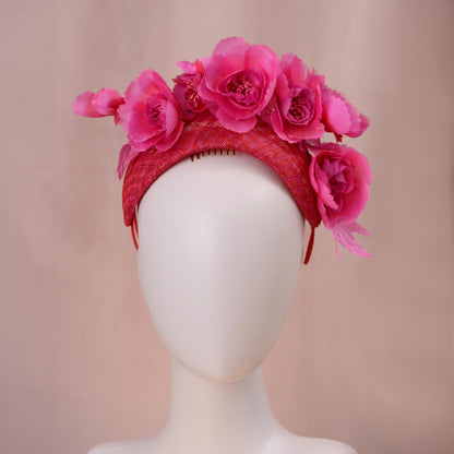 A bright pink and red silk floral fascinator headband displayed on a white mannequin head against a soft beige background.