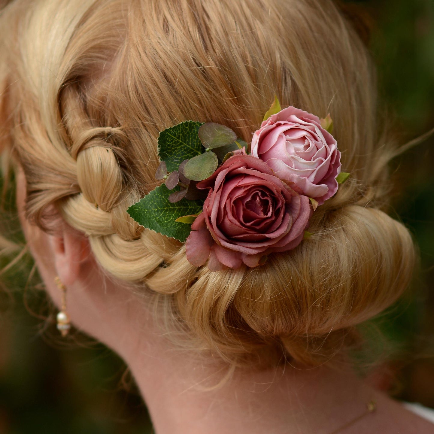 Blonde hair styled in an intricate braid with a flower hair clip  accessory in soft pink roses against a blurred natural background