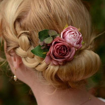 Blonde hair styled in an intricate braid with a flower hair clip  accessory in soft pink roses against a blurred natural background