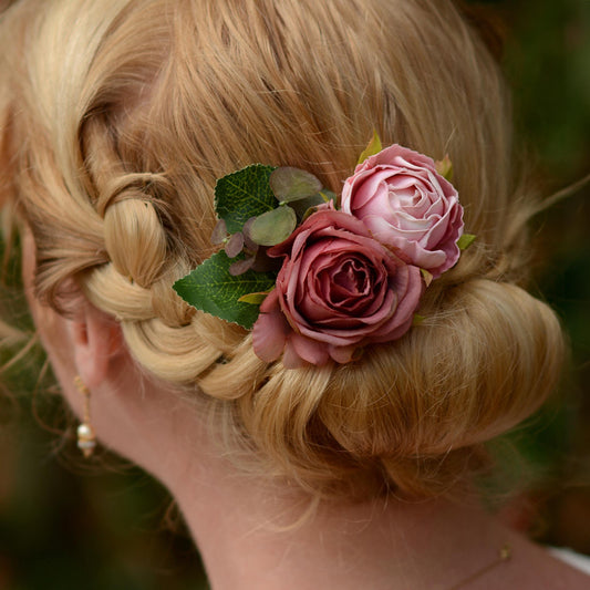 Blonde hair styled in an intricate braid with a flower hair clip  accessory in soft pink roses against a blurred natural background