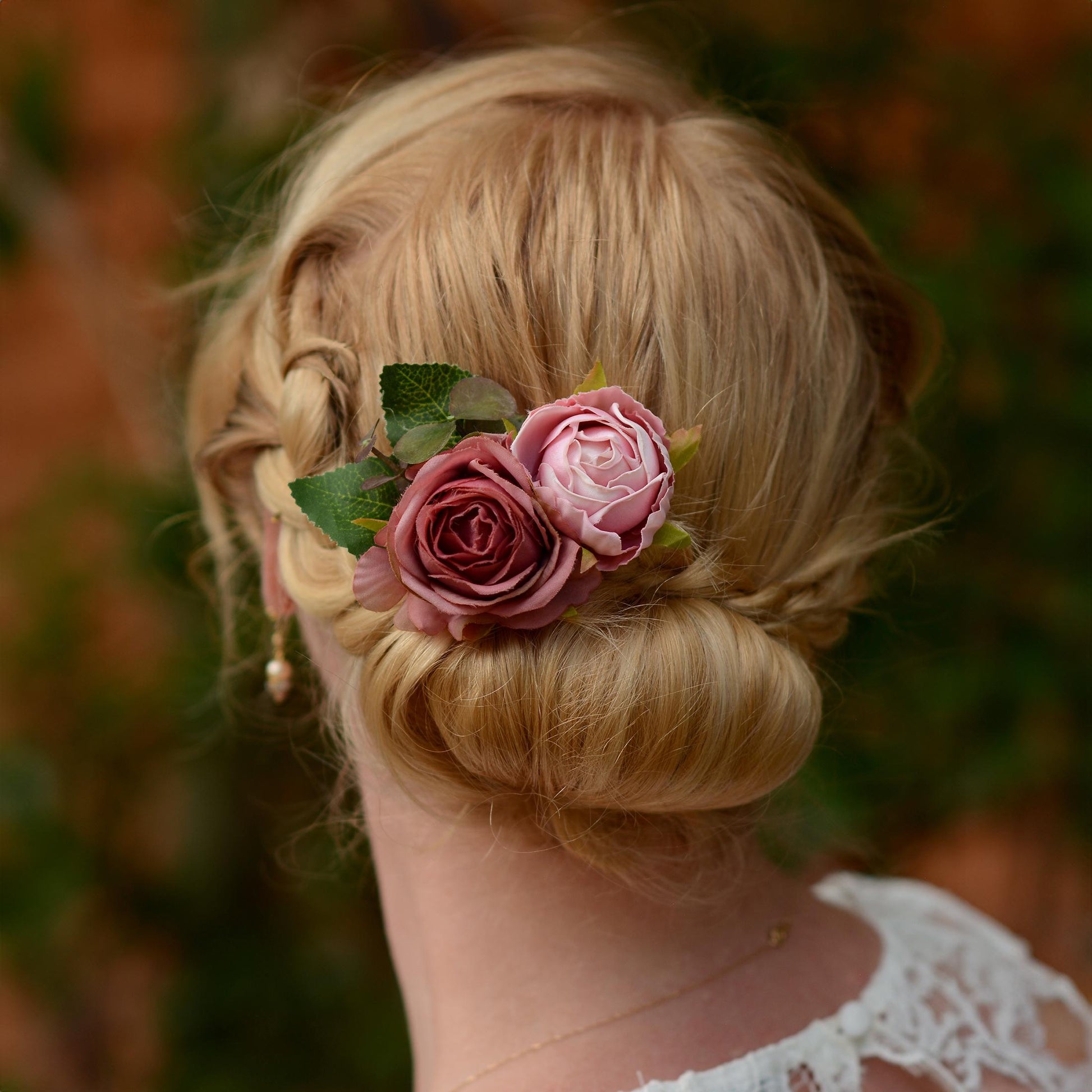 Blonde hair styled in an updo with a flower hair clip  accessory in soft pink roses against a blurred natural background