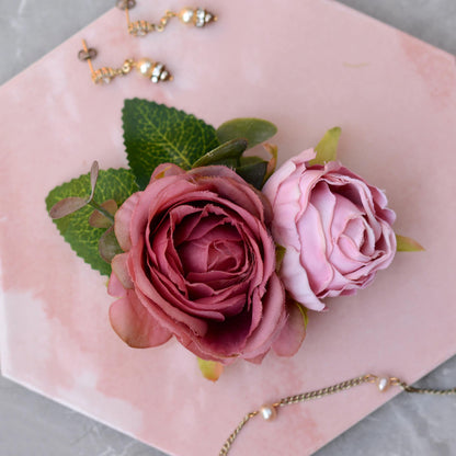 Bridal hair clip of realistic Pink roses with green leaves on a pink surface with jewelry in the background