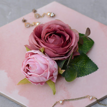 Bridal hair clip of realistic Pink roses with green leaves on a pink surface with jewelry in the background
