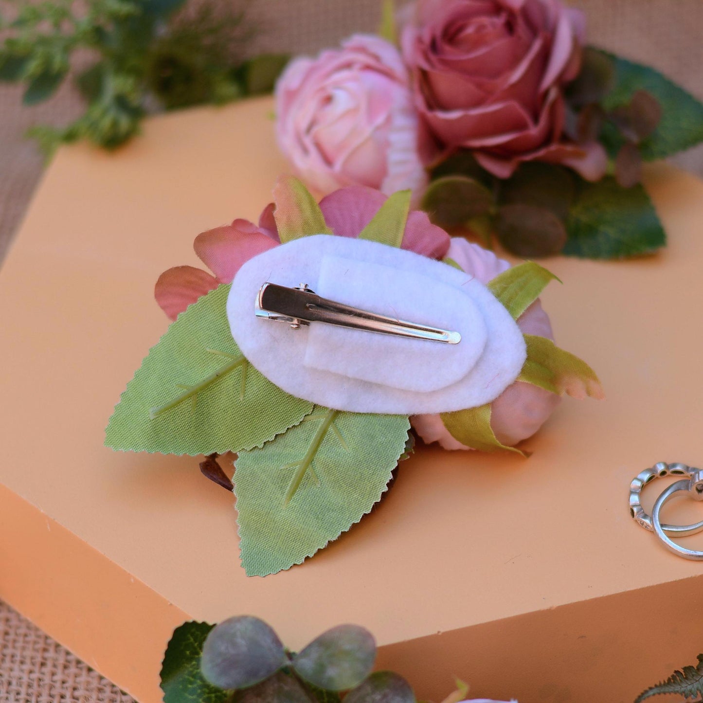Floral hair clip with a barrette on a pink flower and green leaves against an orange background