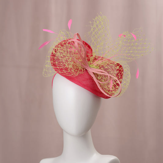 A fuchsia pink-coloured fascinator with a yellow netting overlay and pink feather accents. The hat features a bow and is mounted on a headband. This headpiece is suitable for special occasions, weddings, horse racing and royal garden parties.