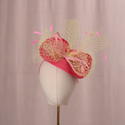  A vibrant tonal pink fascinator, presented on a mannequin head. The hat incorporates a vibrant yellow-green netted veil and is adorned with pink feathers. This headpiece is ideal for formal events and celebrations.