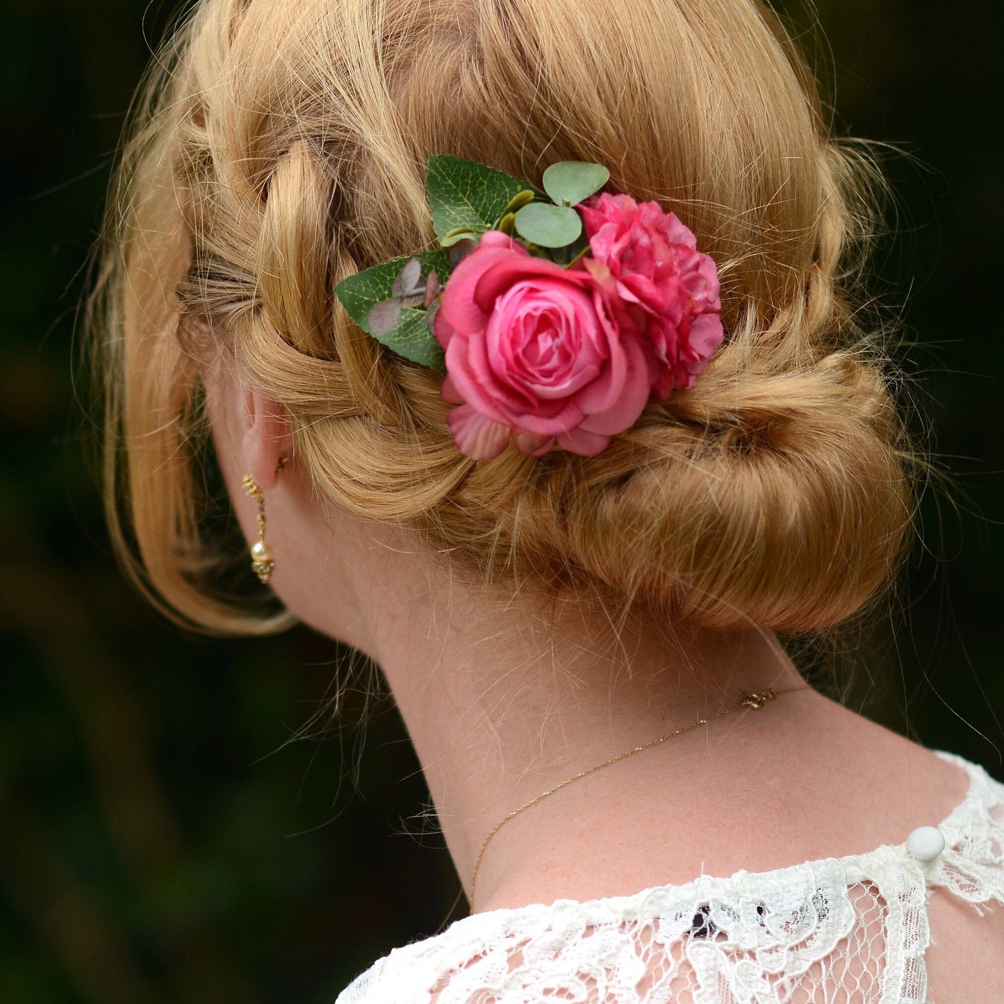 Blonde hair styled in an updo with pink flowers against a dark background