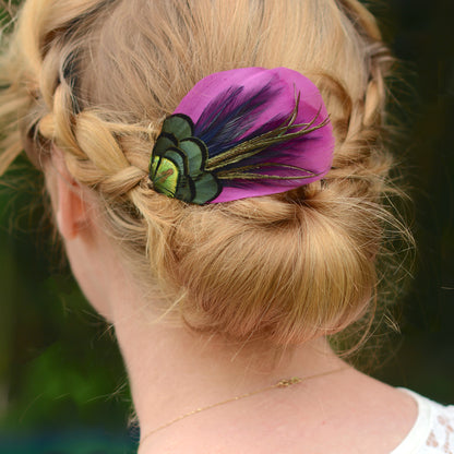 hair clip accessory with purple and green peacock feathers on the back or a woman's head with a braided low bun up-do