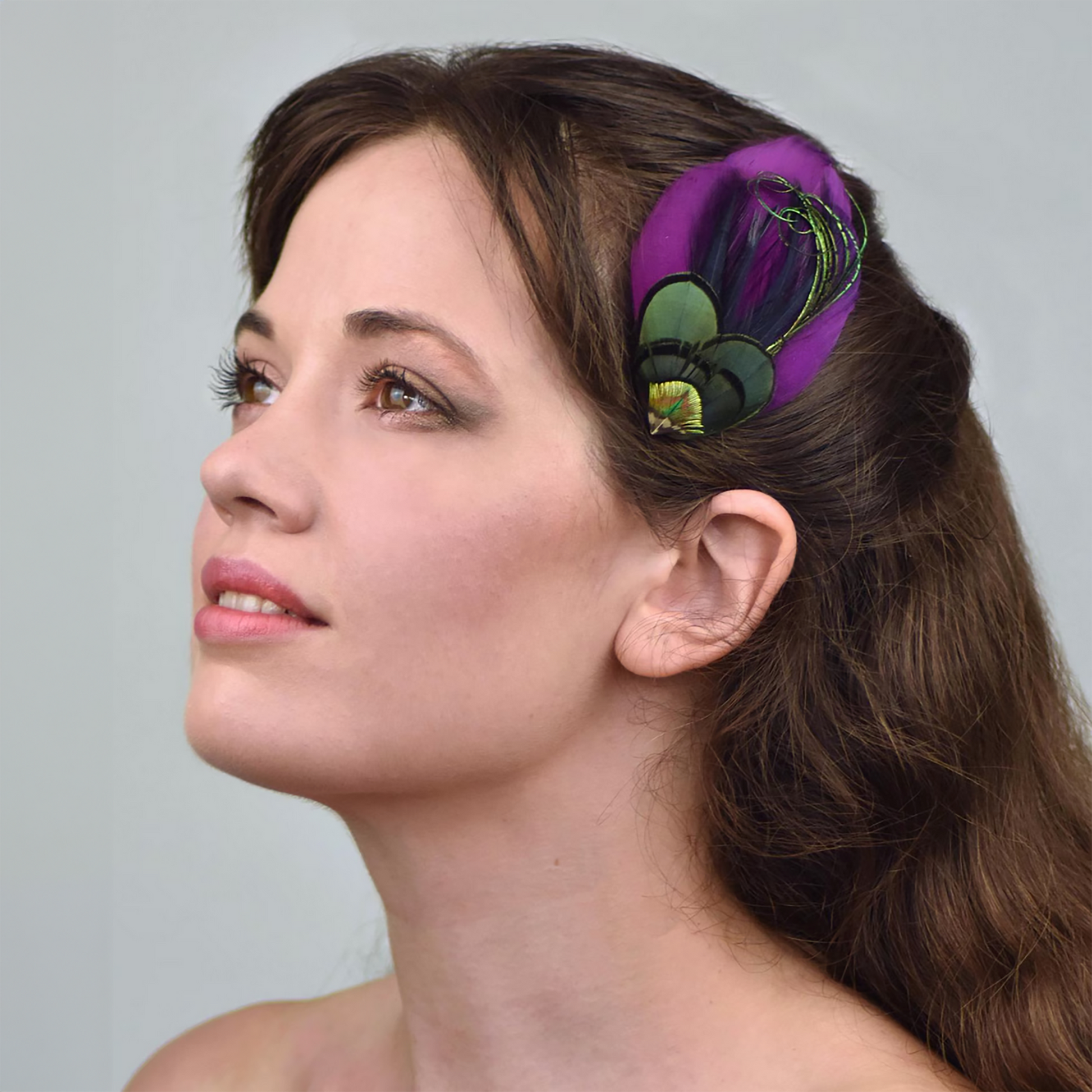 Woman with a purple feathered hair accessory in her hair against a gray background