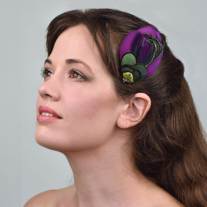 Woman with a purple feathered hair accessory in her hair against a gray background