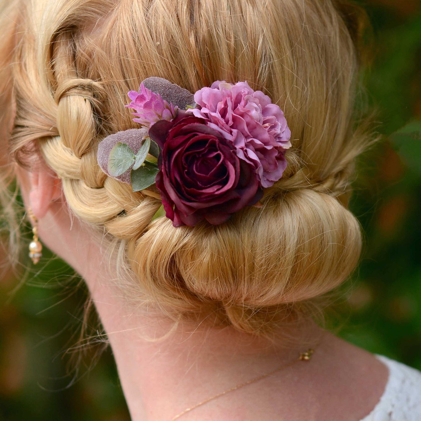 close up of braided hair and low bun decorated with a purple flower hair accessory against a blurred natural background