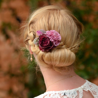Blonde woman with braided hair and low bun decorated with a purple flower hair accessory against a blurred natural background