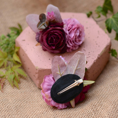Hexagonal pink stone with purple and mauve flower hair accessories on a burlap cloth with green leaves.