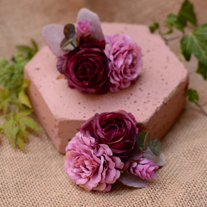 Hexagonal pink stone with purple and mauve flower hair accessories on a burlap cloth with green leaves.