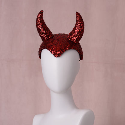 Red sequined theatrical red devil horn headband displayed on a white mannequin head against a soft pink backdrop.