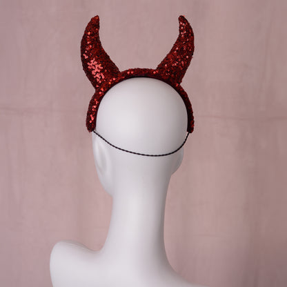 Red sequined devil horns headband with a black hat elastic, displayed on a white mannequin head against a soft pink backdrop.