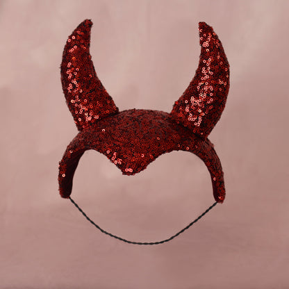 A red sequined devil horn headband headpiece with a black hat elastic, shown against a solid dusty pink background.
